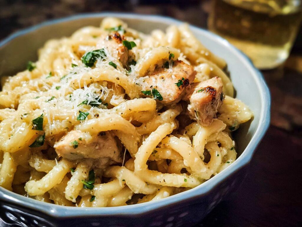 A bowl of creamy garlic parmesan chicken pasta topped with shredded cheese and parsley.