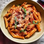 A close-up of a bowl of creamy tomato basil pasta, topped with Parmesan cheese and fresh basil leaves.