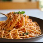 A fork lifting a swirl of creamy tomato basil pasta, garnished with fresh basil leaves.