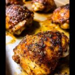 Close-up of perfectly baked juicy chicken thighs with crispy skin and herbs.