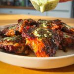 Close-up of juicy baked chicken thighs, glistening with a herb and cheese topping, served on a plate.
