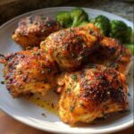 Close-up of juicy baked chicken thighs seasoned with herbs, served with steamed broccoli.