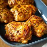 Close-up of perfectly baked, juicy chicken thighs seasoned with herbs in a blue baking dish.