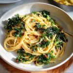 Close-up of spaghetti with wilted kale, red chili flakes, and grated cheese, a fork rests on the side.