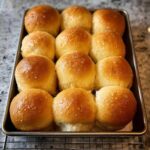 A baking pan filled with golden brown, fluffy Thanksgiving dinner rolls, glistening with butter.