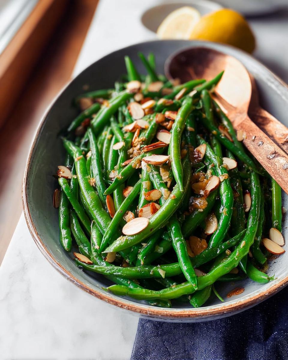 A close-up of bright green beans tossed with slivered almonds and a light dressing, presented as a cozy Thanksgiving side dish.