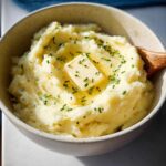 Close-up of creamy mashed potatoes topped with melting butter and fresh chives, a perfect Thanksgiving side dish.